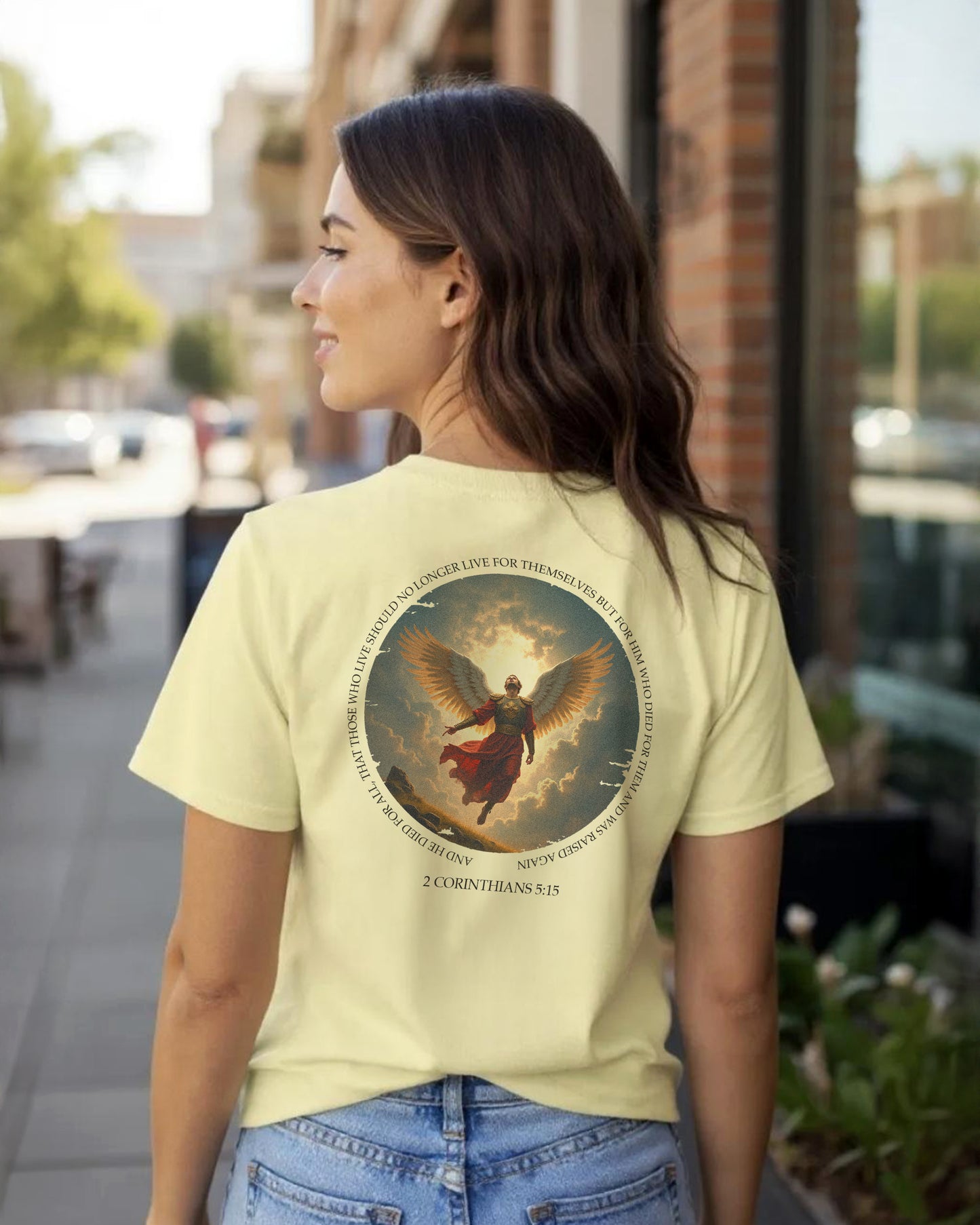 Woman wearing a light yellow t-shirt with a charlie kirk graphic design on the back, standing outdoors.